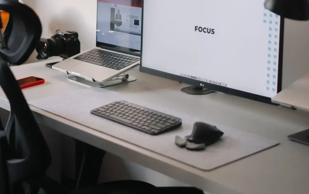 Home office desk with laptop stand, monitor, keyboard, camera, and headphones