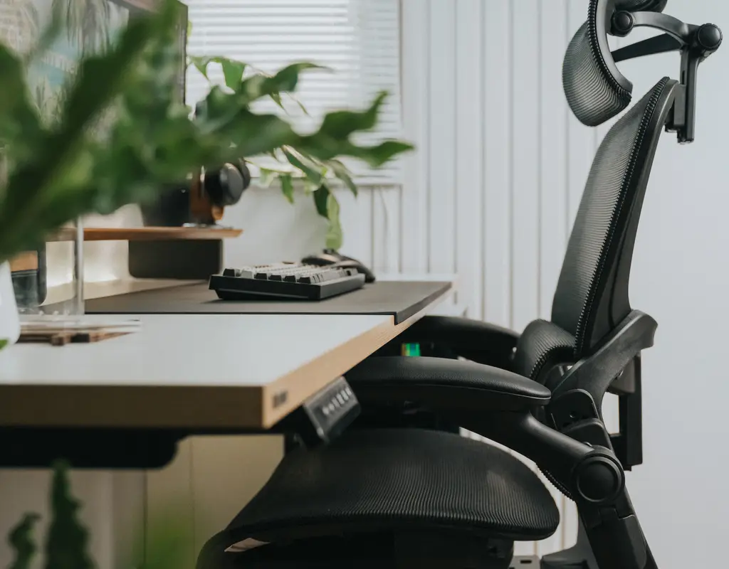 Black mesh ergonomic office chair beside a desk with keyboard and plants