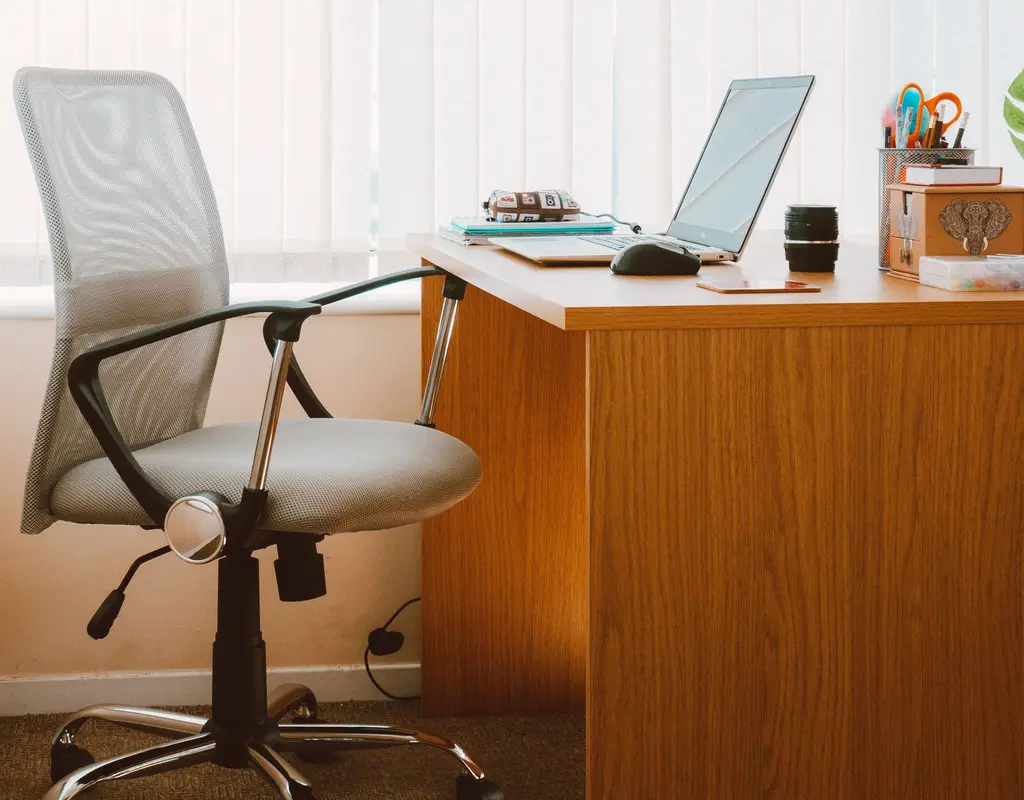 Gray mesh office chair positioned beside a wooden desk with laptop