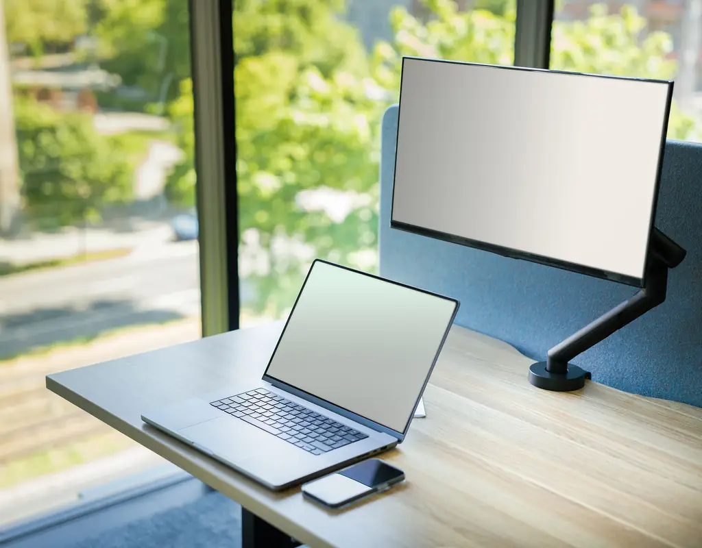 	Clamp-on monitor arm mounted to desk edge with laptop nearby