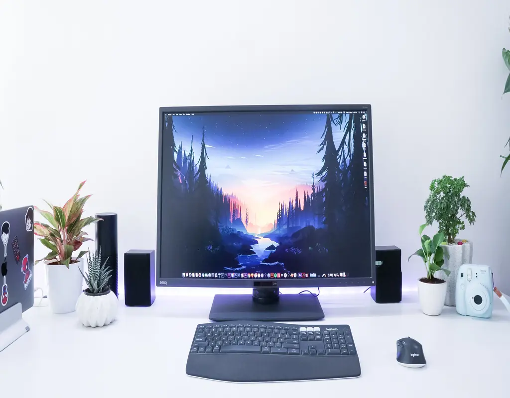 A BenQ monitor on a clean white desk with plants and speakers