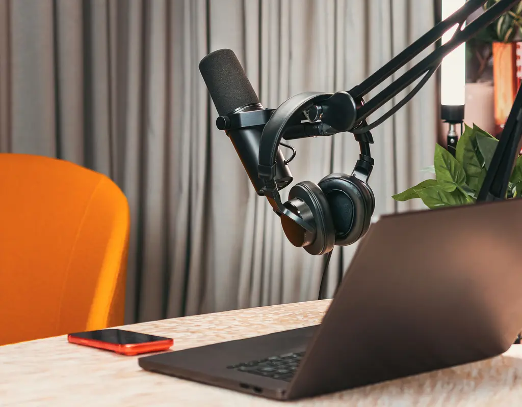Microphone and headphones on a boom arm beside a laptop in a home office