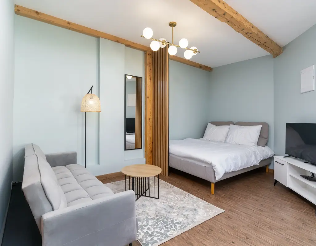 Small bedroom with multi-functional furniture including a sofa bed, built-in mirror, and compact TV console