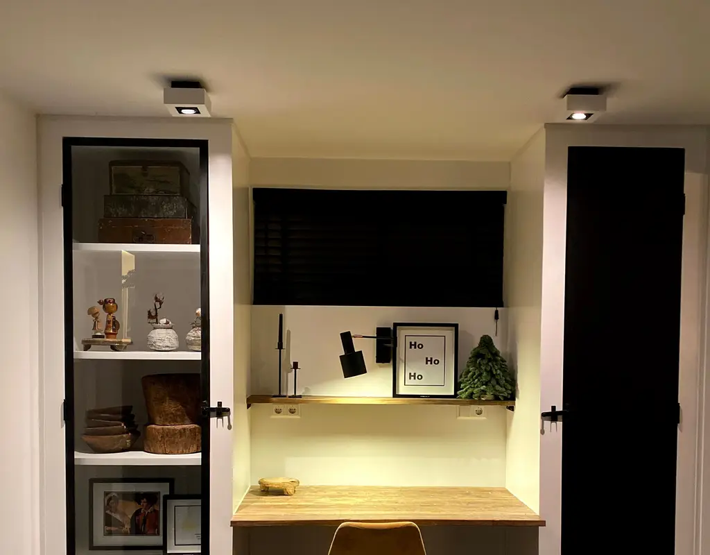 Alt Text: Small home office nook with layered lighting — ceiling spotlights, an adjustable task lamp, and warm under-shelf ambient light